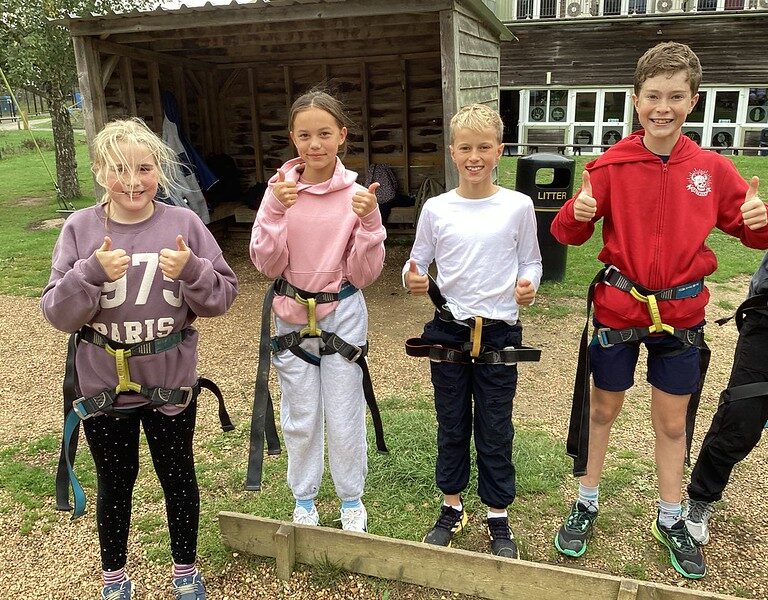 four children wearing harnesses, posing with their thumbs up