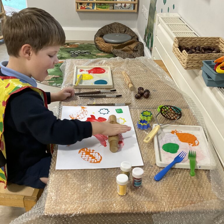 young boy rolling a rolling pin over some paints