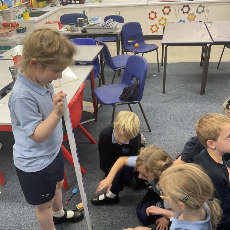 group of school kids in a classroom measuring the height of a ball