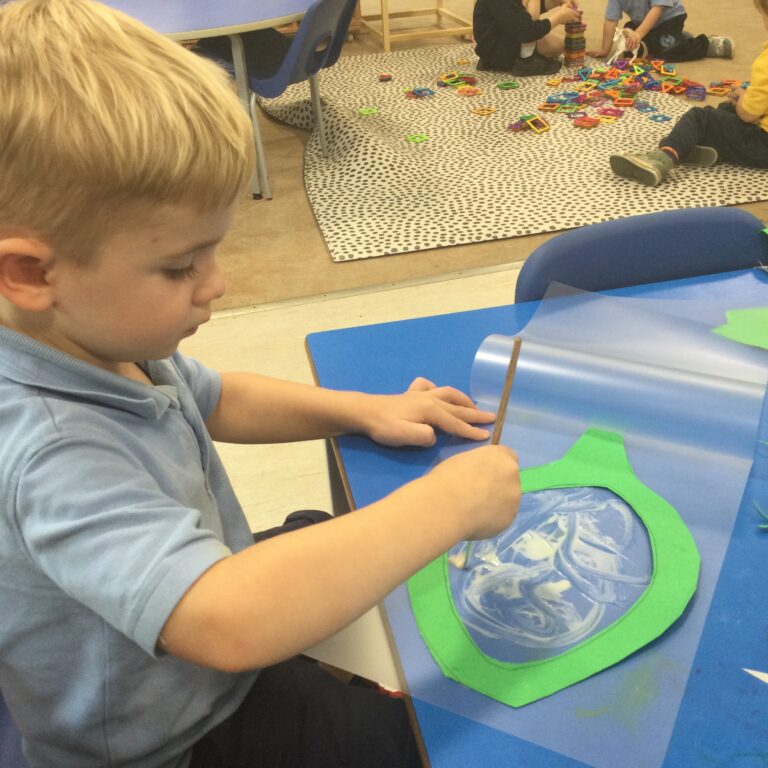 little boy spreading glue around with a paintbrush
